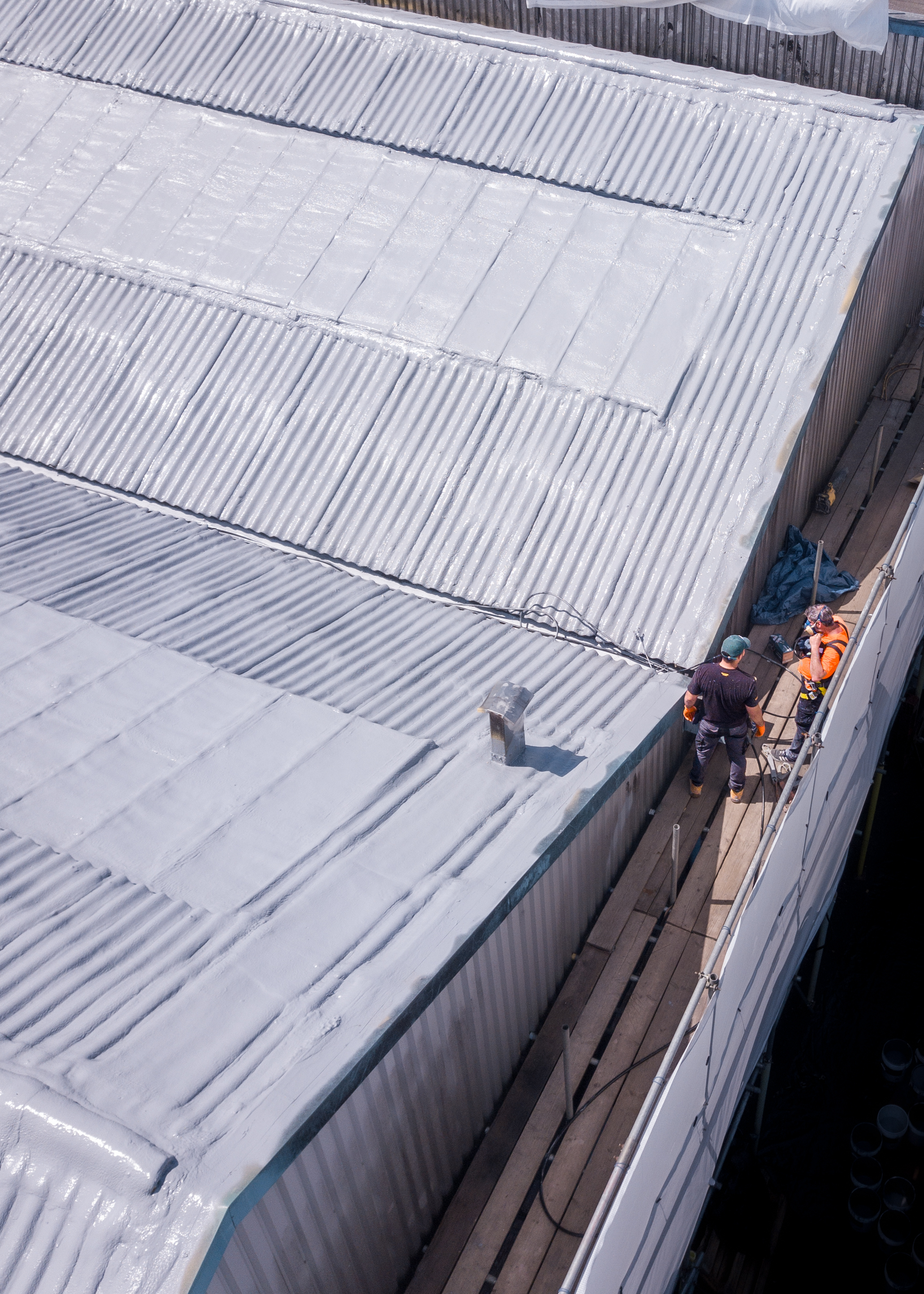 Operatives applying Gaco silicone coating to asbestos cement sheets